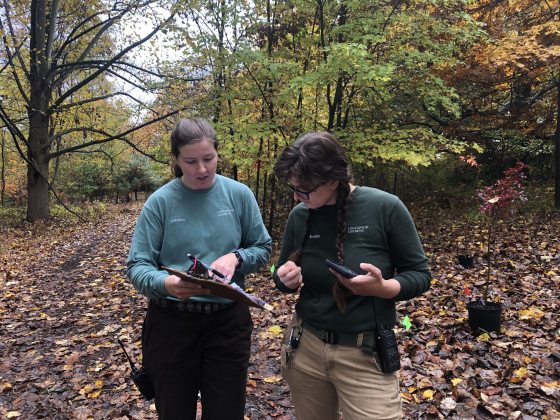 two people standing next to each other, one holding a clip board and the other person looking at it